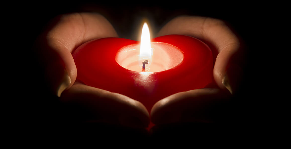 woman's hands holding a heart shaped candle in the dark